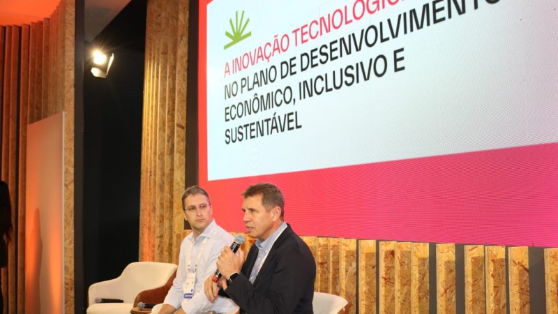 Fotos de dois homens brancos , um usando camisa branca e outro usando terno preto. O de terno preto fala ao microfone.