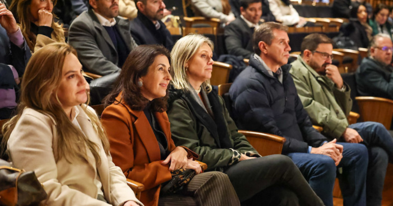 Pessoas sentadas na plateia olham para frente com expressões agradáveis