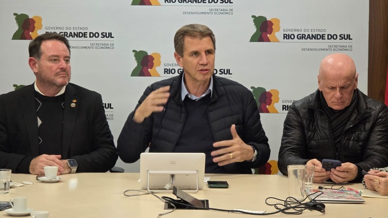 Três homens brancos sentados lado a lado. Há um tablet na frente deles.