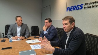 Foto de três homens brancos sentados ao redor de uma mesa