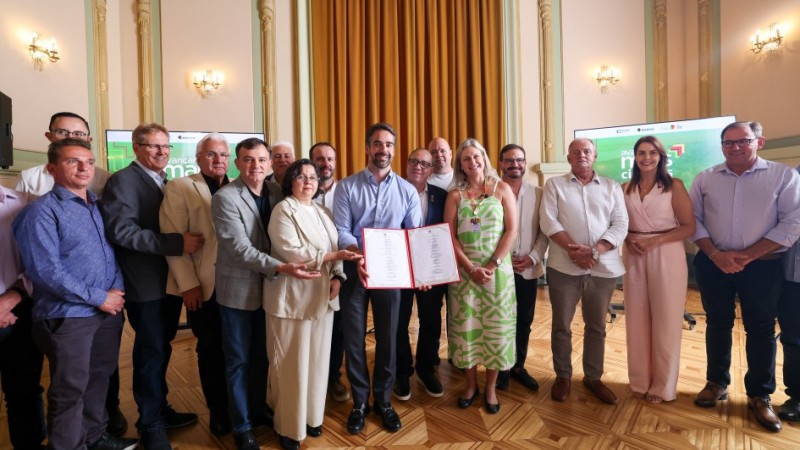 Foto de um grupo de pessoas, de p&eacute;, posando para a foto. As do meio seguram um documento aberto.