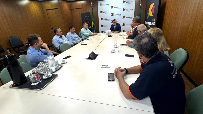 Imagem de uma mesa longa de reuni&otilde;es, bege, com pessoas sentadas ao redor