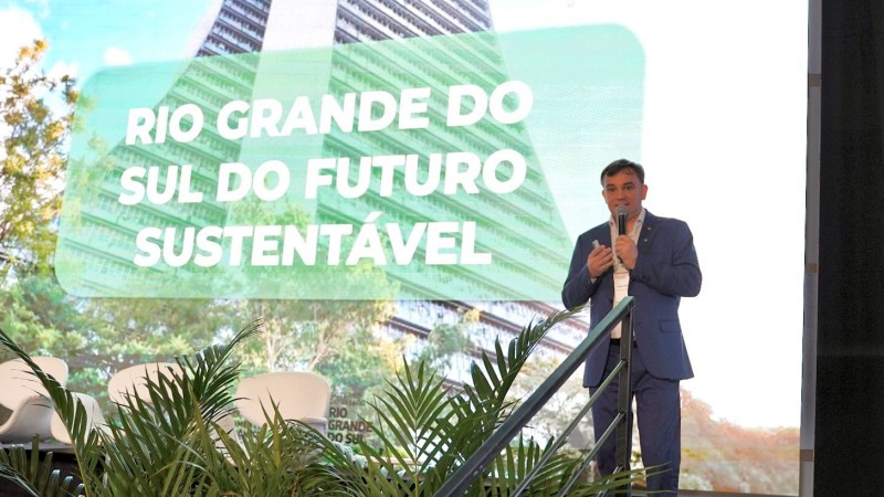 Foto do secret&aacute;rio Leandro Evaldt, que usa terno azul, em frente a um tel&atilde;o onde se l&ecirc; "rio grande do sul do futuro"