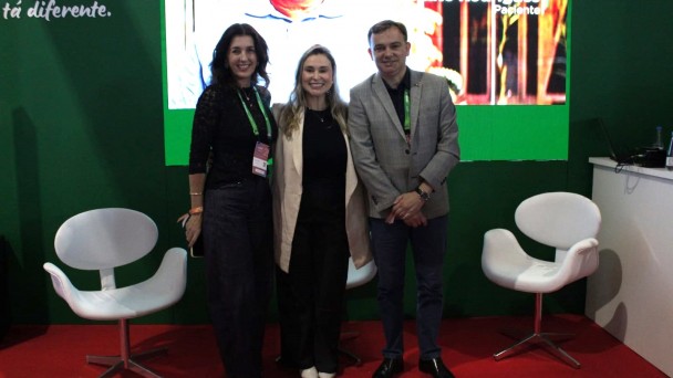 tr&ecirc;s pessoas, duas mulheres e um homem, de p&eacute;, em um palco com fundo verde